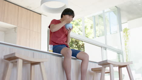 teenage asian boy enjoys a bowl of cereal at a modern home kitchen