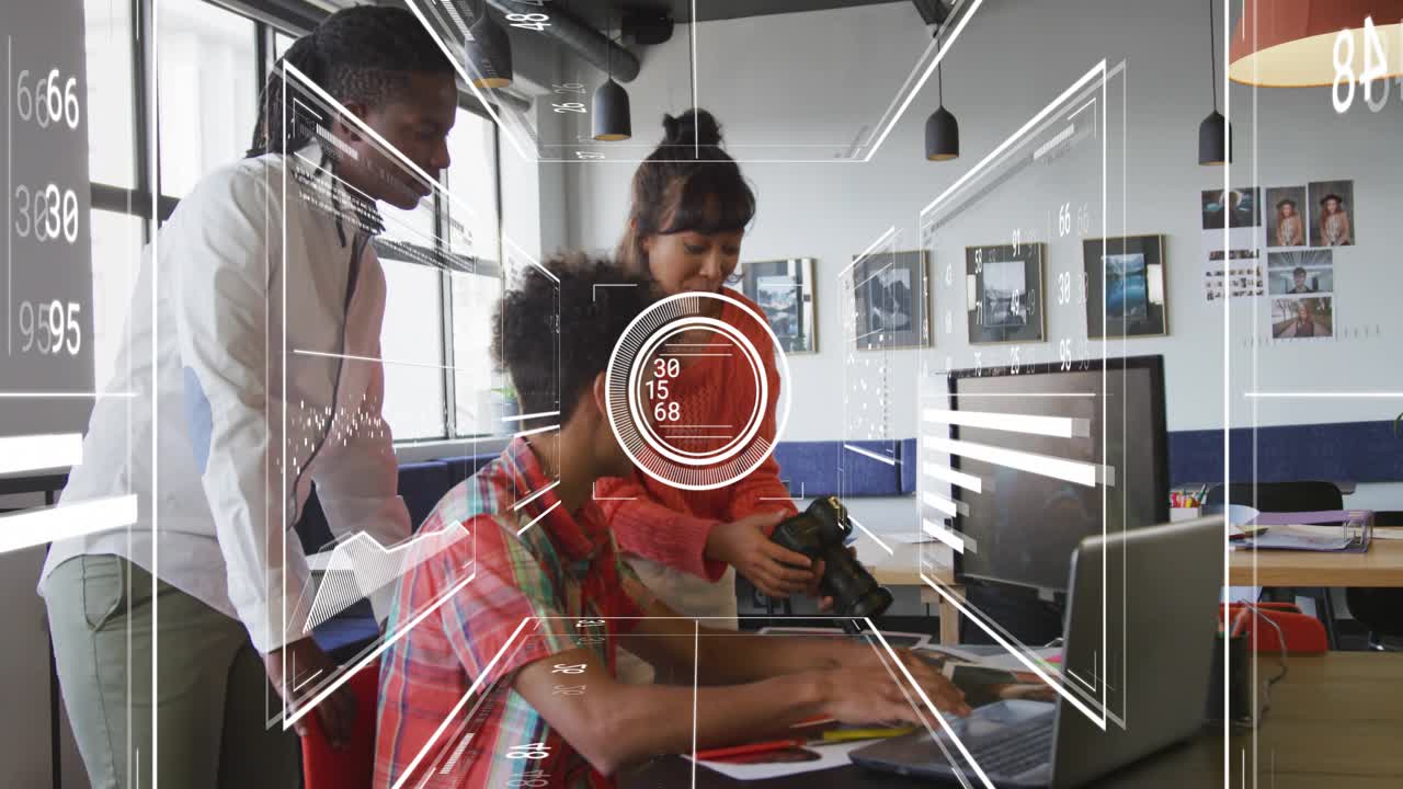 Woman gesturing, grabbing DSLR, man typing laptop, HUD animating targets over team for tech editing