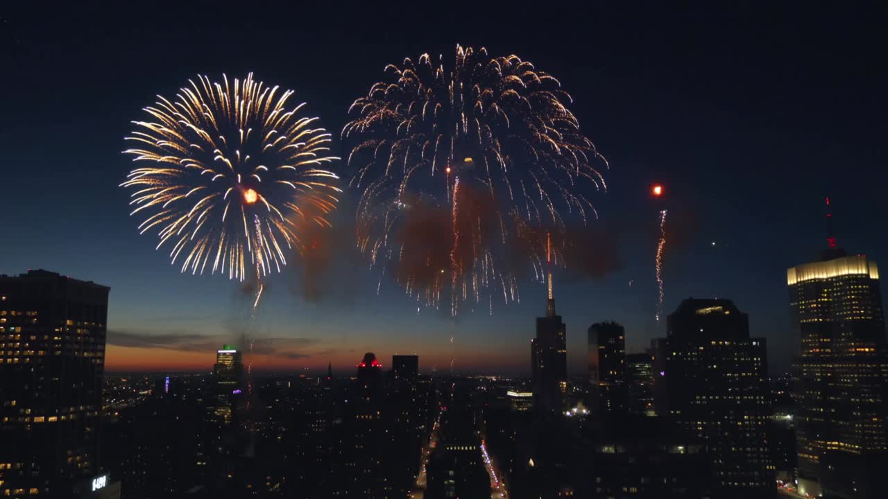 Lighting shells bursting with spark fountains over streets and towers at dusk, making golden blooms