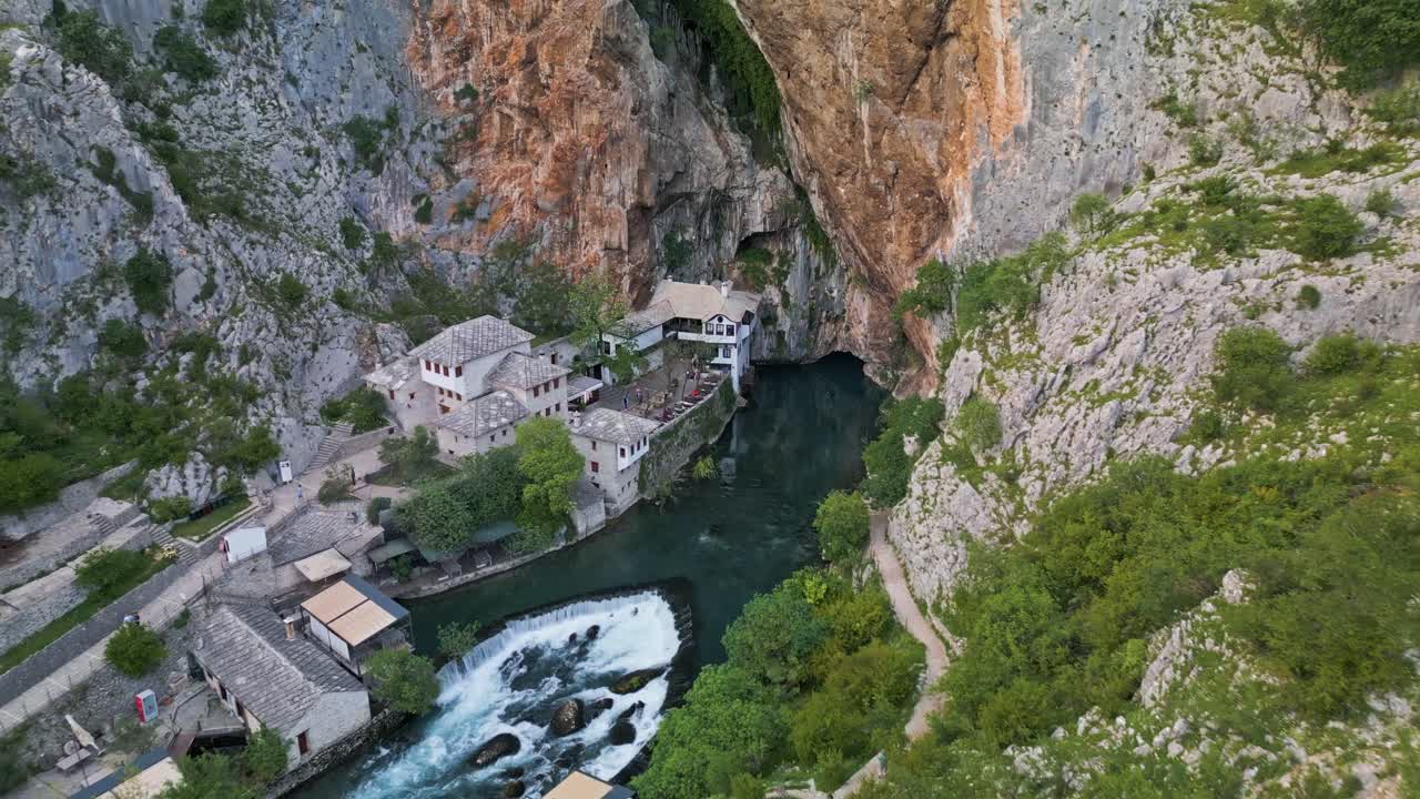 Drone shot pulling out from Blagaj Monastary in Mostar, Bosnia showing the surrounding countryside and moutain it's built under. A river running under a mountain with the building built into the rocks
