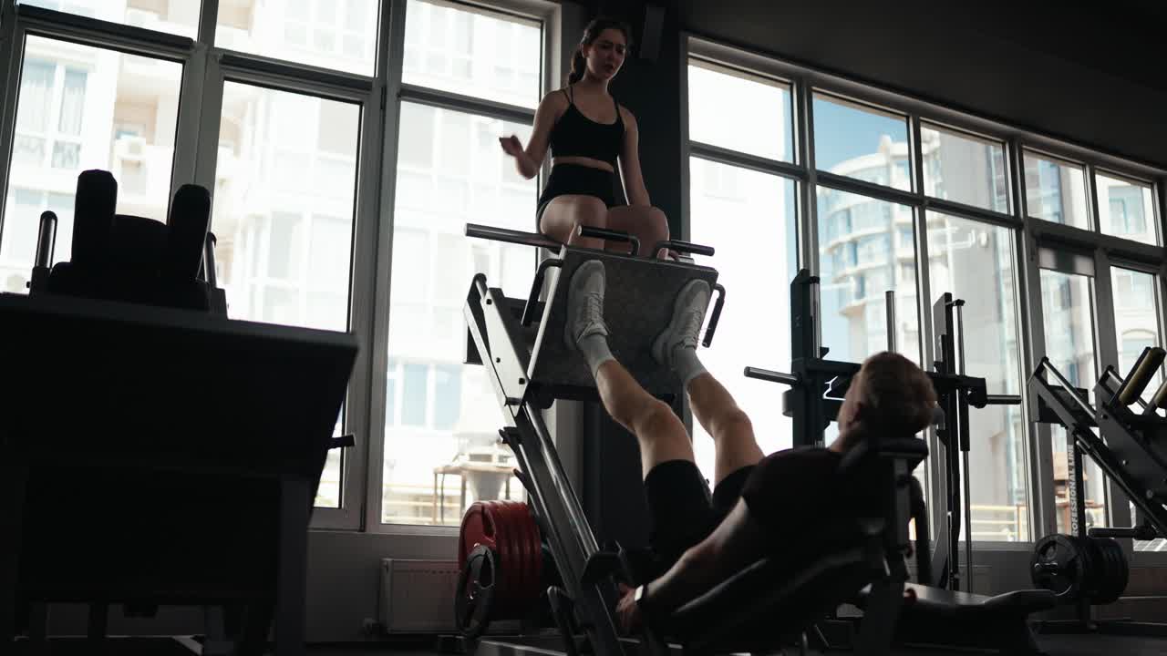 Donna che aiuta un uomo con l'allenamento di leg press in palestra