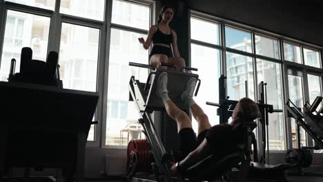 mujer ayudando a un hombre con ejercicios de presión de piernas en el gimnasio