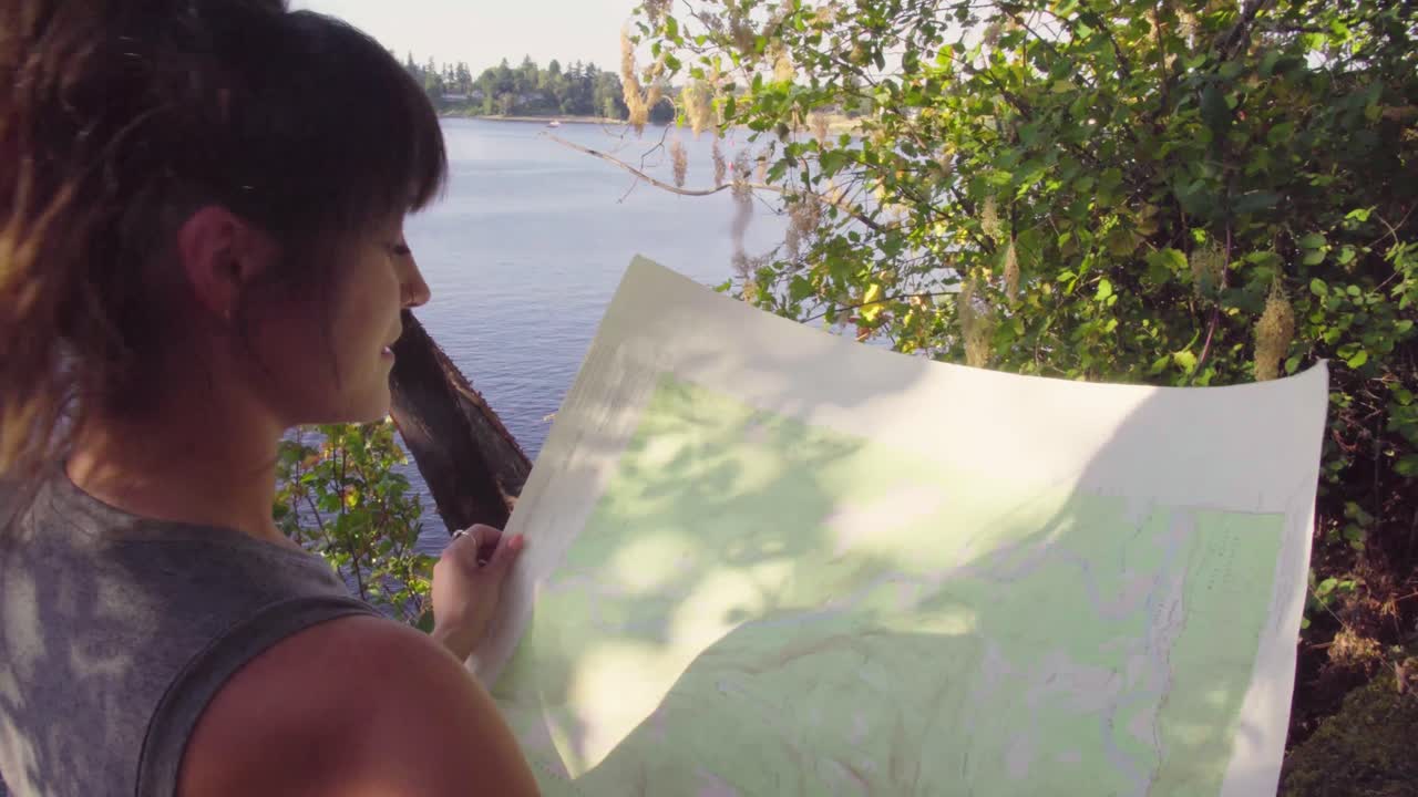 그녀가 있는 공원의 지도를 읽고 보고 있는 귀여운 힙스터 소녀의 어깨 너머로 핸드헬드 영상