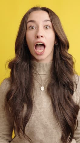 young woman showing surprise and excitement on yellow background
