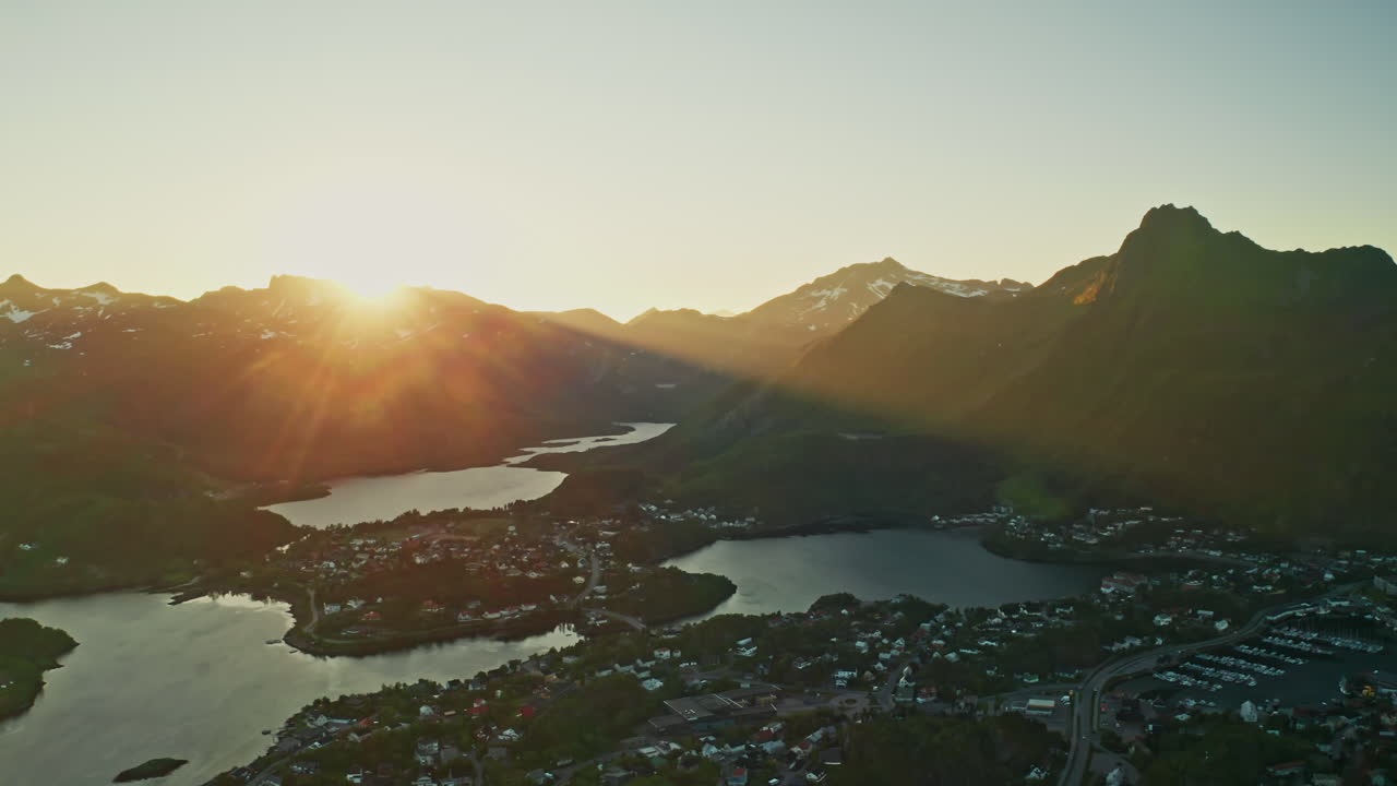 Aerial drone shot over the Norwegian town of Svolvaer in the Lofoten Islands, Norway. Bird's eye view of the fishermen's town at the midnight sun. View of the vast mountains in the background.
