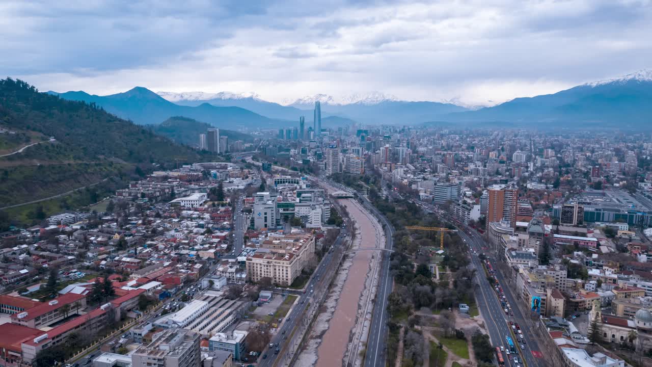 Hyperlapse aereo in allontanamento con centro direzionale al centro e skyline nuvoloso con catena montuosa delle Ande innevate, traffico veicolare intenso