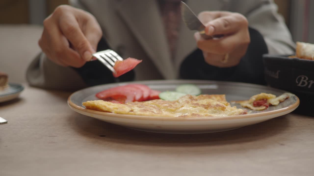 Detailní záběr osoby krájející omeletu vidličkou a nožem