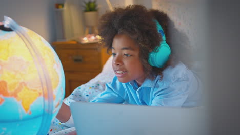 boy in bedroom lying on bed using with laptop with illuminated globe