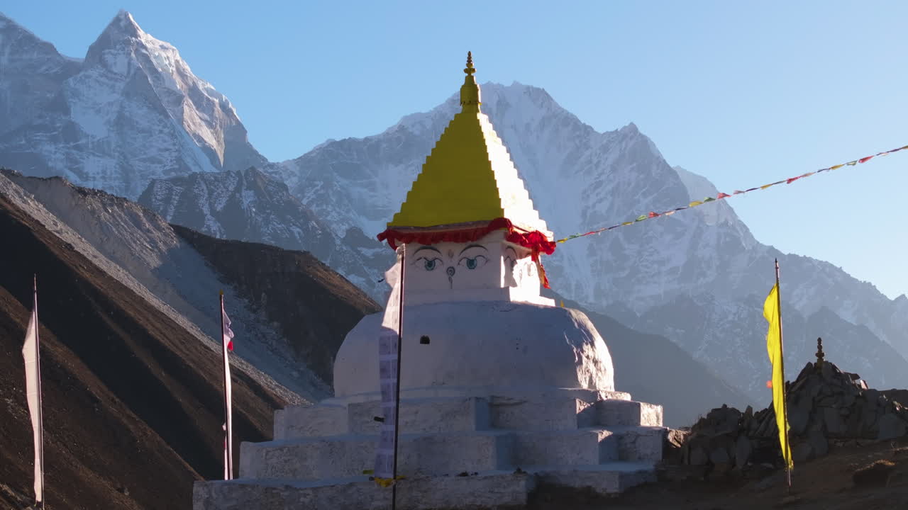 Langsomt glidende luftdroneoptagelse, der gradvist afslører Himalaya-bjergene bag en hvid buddhistisk stupa i Dingboche, Nepal. Bedeflag og fredfyldt højtliggende landskab i Everest-regionen