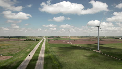 slow aerial rise over wind turbines in sunny fields, traffic on straight highway.
