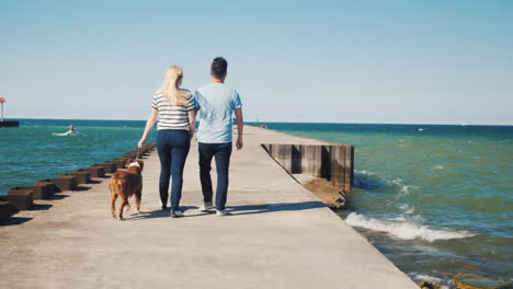 young multiethnic couple walks with a dog on a pier