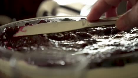 untando una gruesa capa de deliciosa mermelada y mermelada encima de un enorme pastel de queso con un cuchillo
