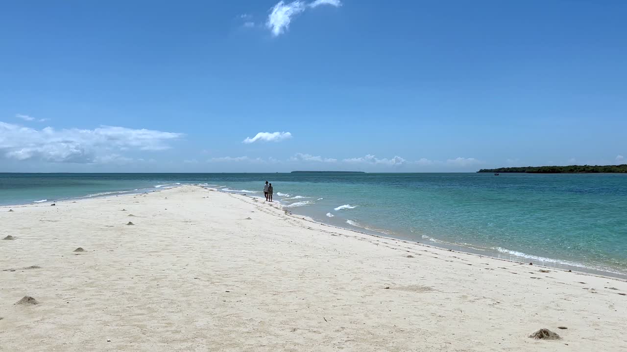 Couples walking on a white sandy beach in Zanzibar. Tanzania.