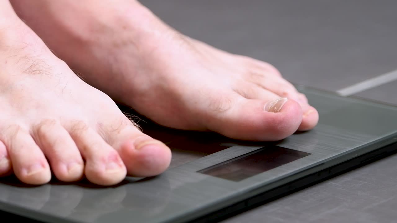 el hombre se sube a una báscula casera, comprueba su peso y retrocede