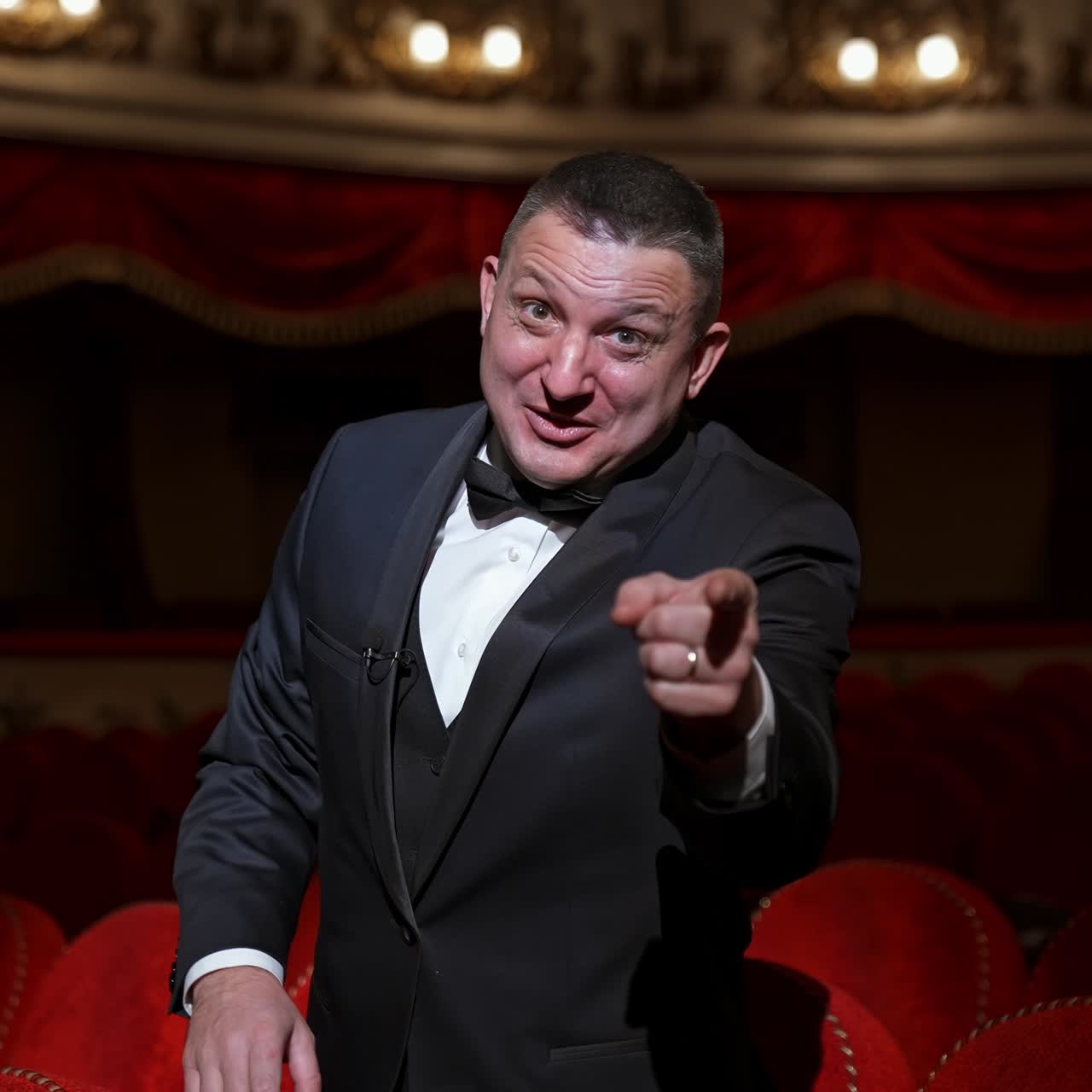 Man in empty theater hall points on a hand with watch and waits for performance beginning. Ready to watch visitor