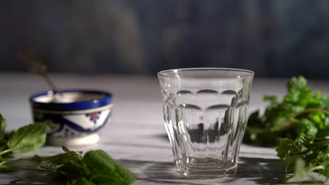 cámara lenta, ángulo alto, toma ajustada de la mano recogiendo una tetera ornamentada y vierte té en un vaso con un tazón marroquí y menta alrededor