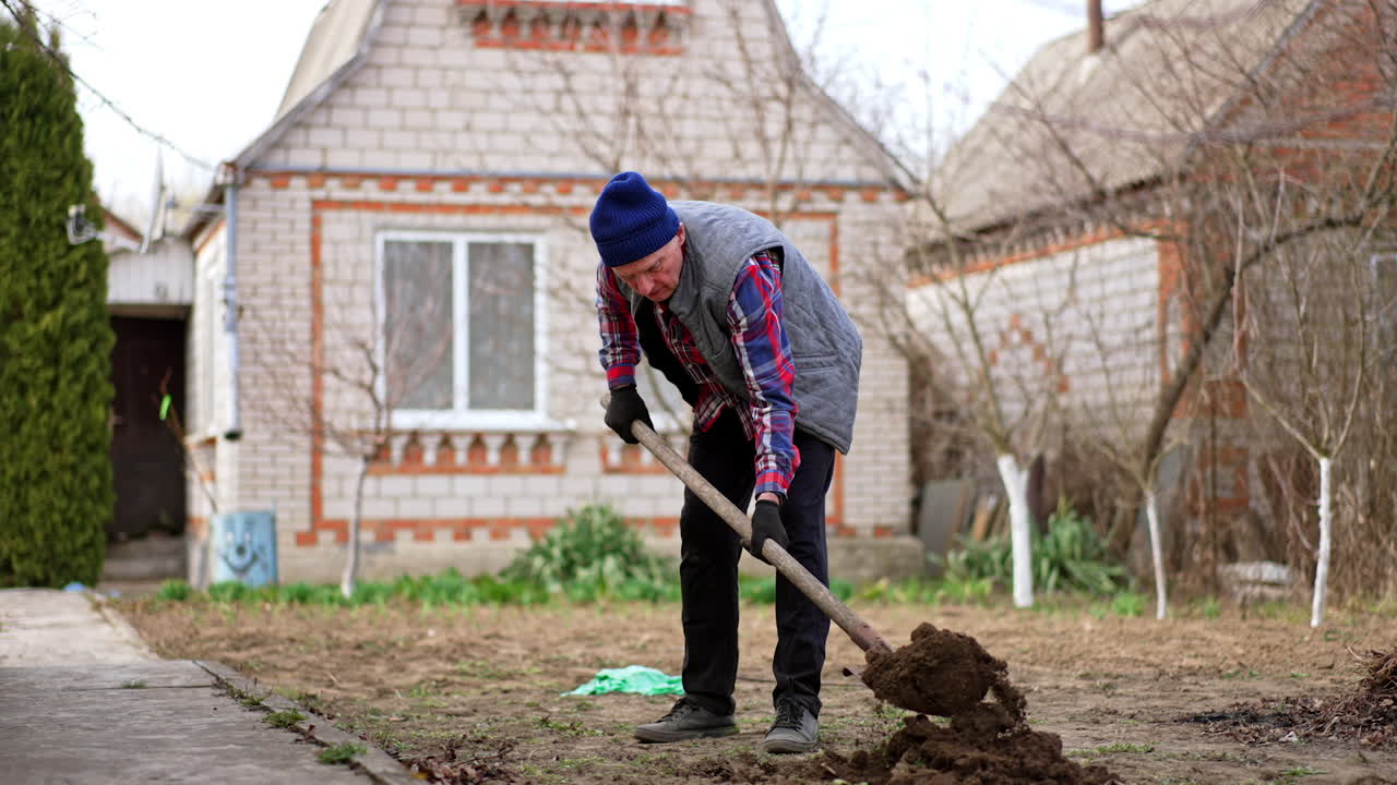 Mature Caucasian man working in the garden digging a hole in the ground. Farmer planting trees near his house.