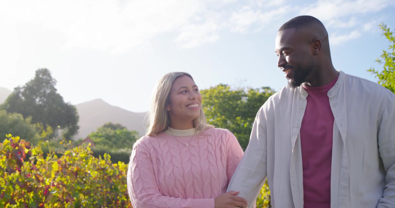 African American couple linking arms walking in garden among shrubs smiling and appreciating view