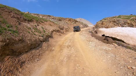 pov following a 4wd vehicle going up black bear pass trail, past rocky hills and dirty snow drifts in san juan mountains near telluride colorado