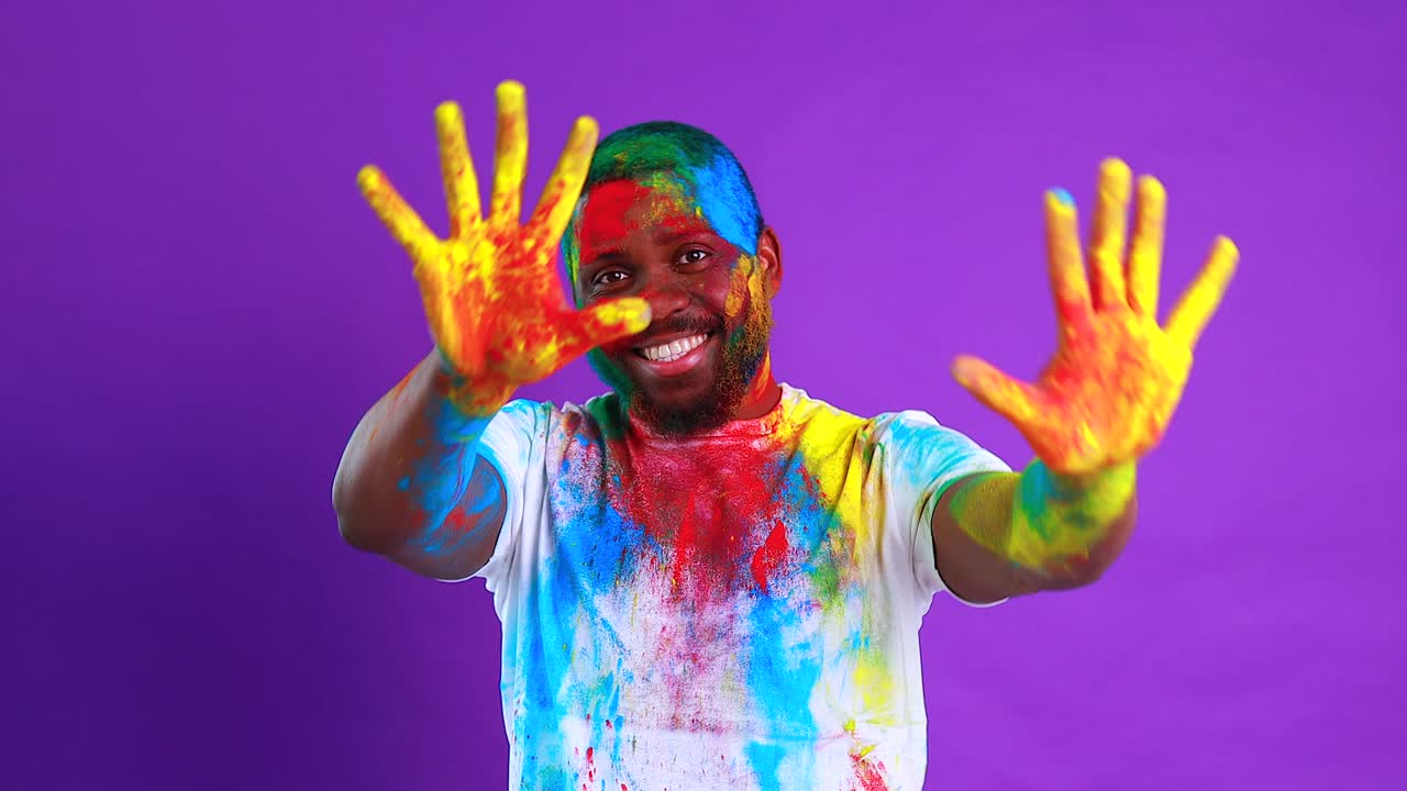 Afro american man celebrate holi festival in violet studio background