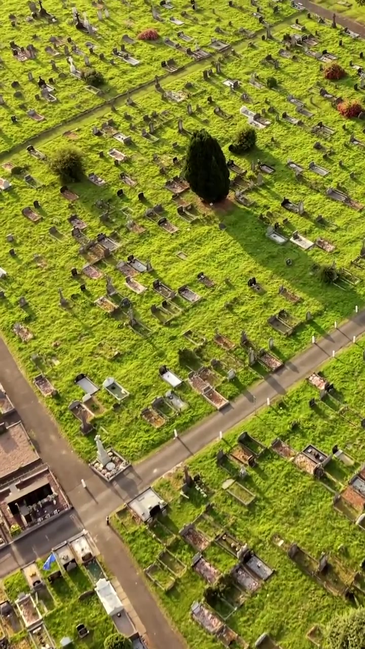 Wide overhead aerial video of Milltown Cemetary in West Belfast, Northern Ireland on a bright summer evening. Produced in 60FPS, 1080x1920 social ratio and with Rec709 colour.