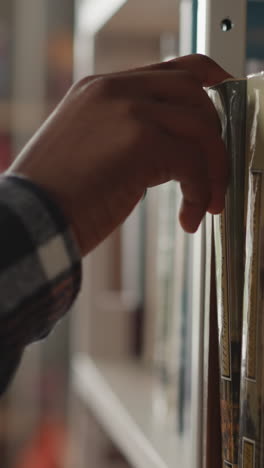 un hombre recoge con la mano un libro del estante en un primer plano de la biblioteca. un lector afroamericano busca literatura para prepararse para exámenes en el centro de información. hobby de lectura