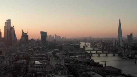 Toma-Aérea-Sobre-El-Río-Támesis-Hacia-Los-Rascacielos-De-Londres-Al-Amanecer