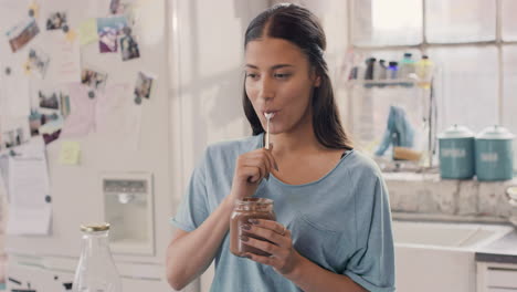 pretty hispanic girl eating chocolate spread using spoon from jar