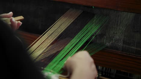 woman adjusts shuttle after weaving through loom, pulls to close loom