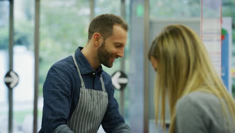 una fotografía auténtica de una cliente feliz sonriendo mientras habla con un amigable cajero masculino que está escaneando y comprobando productos alimenticios en el supermercado.