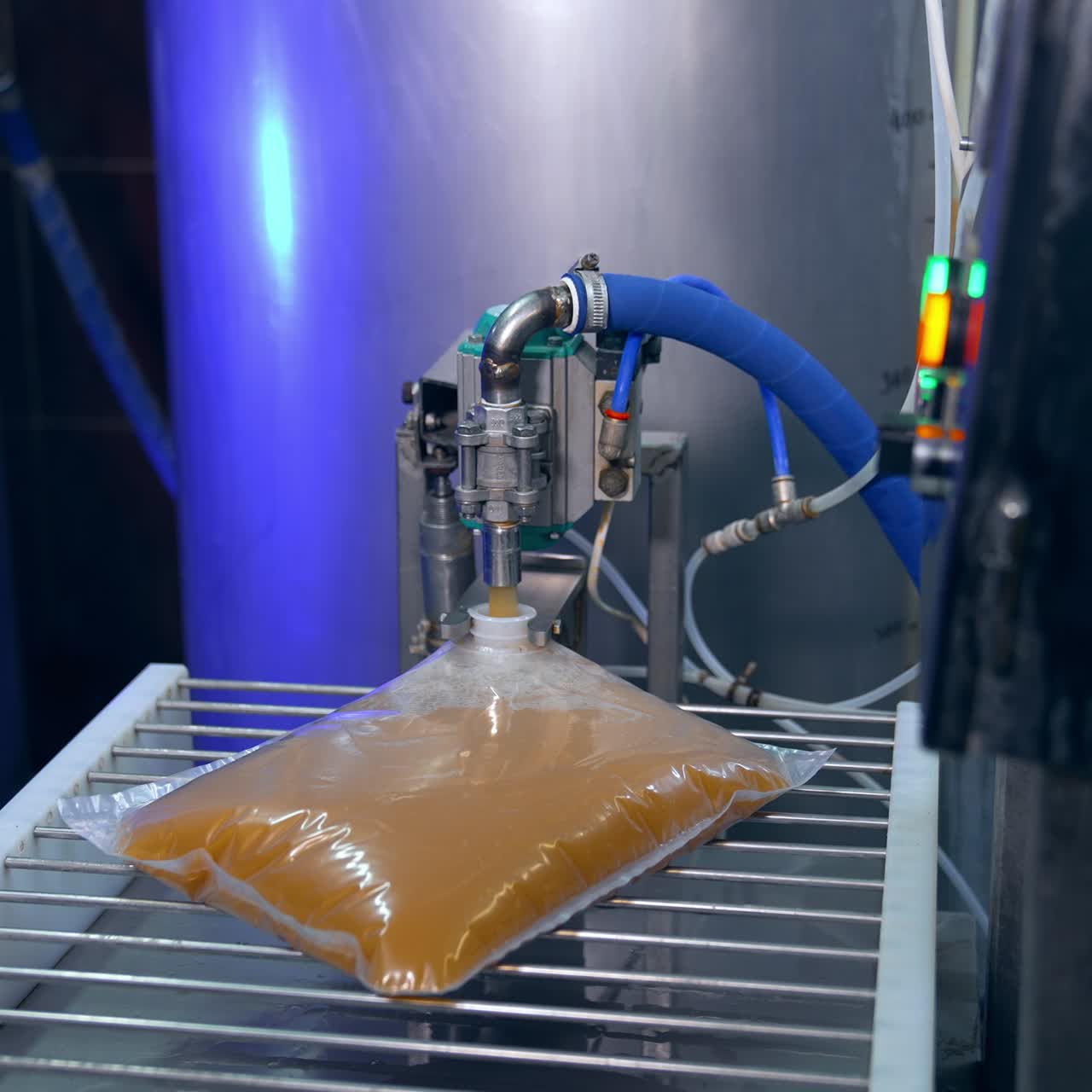 Freshly-made apple juice poured into the plastic bag. Packaging of organic product into a pack. Food factory worker takes the filled bag away