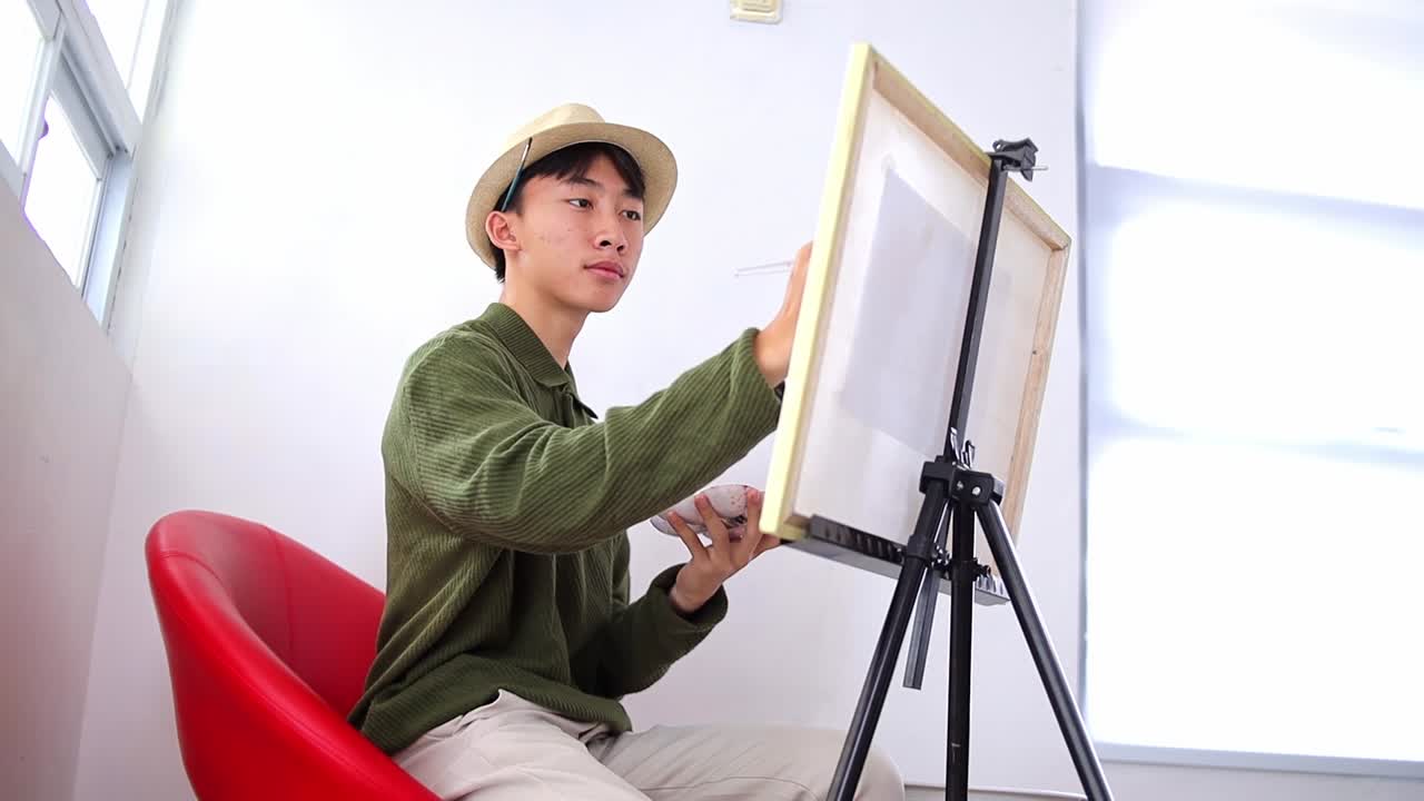 Focused young asian artist creating expressive artwork on canvas with passion and skill