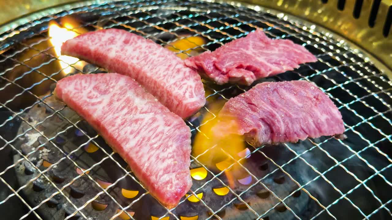 Primo piano di manzo marmorizzato di alta qualità che cuoce su una griglia a filo con fiamme arancioni tremolanti