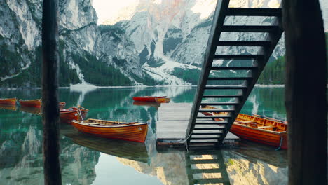 passing under a boathouse and out over a dock and across the pristine waters of lago di braies, italy, aerial