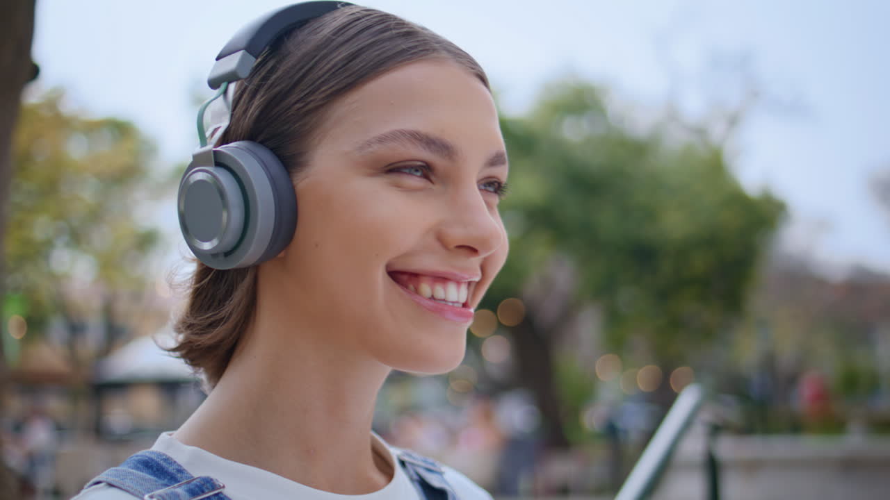 Cheerful zoomer listening music in headphones at street feeling joyful closeup