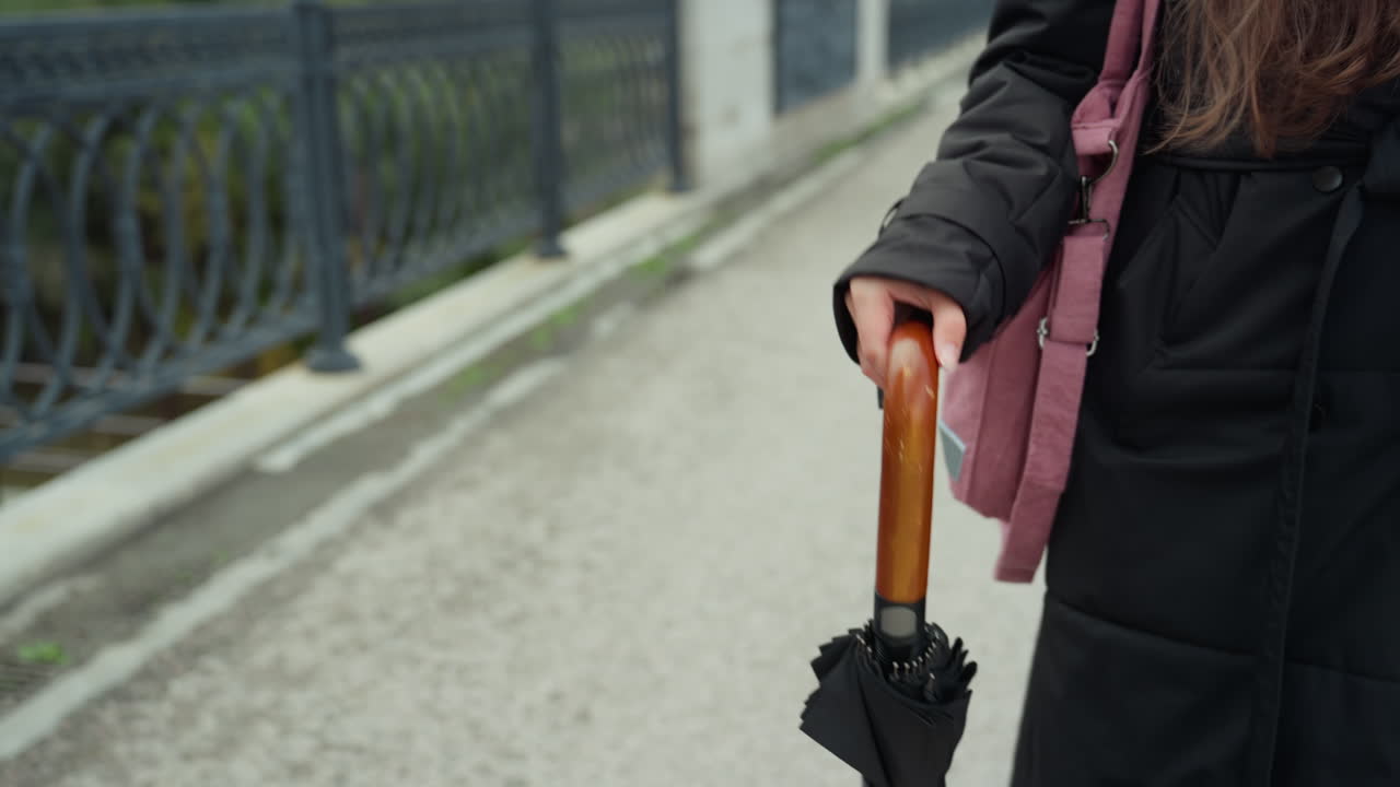 Bro, gangvei, paraply og rosa ryggsekk krysser kanal. Kvinne pendler langs rekkverk med paraplyhåndtak i tre. Våte fortau, refleksjoner og overskyet himmel skaper en målrettet by