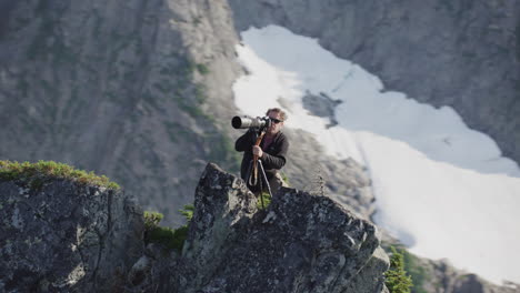 photographer double checks camera view on mountain ridge, medium tracking helicopter counterclockwise orbit slow motion