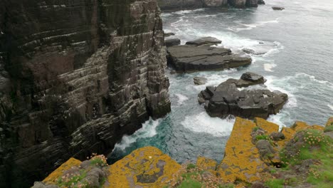 Una-Toma-De-Inclinación-Lenta-Se-Eleva-Suavemente-Para-Revelar-Una-Colonia-De-Aves-Marinas-En-Un-Acantilado-Espectacular-Y-Escarpado-Mientras-Las-Olas-Verde-Turquesa-Chocan-Contra-La-Base-Del-Acantilado