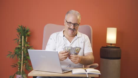 un anciano mirando una computadora portátil contando dinero.