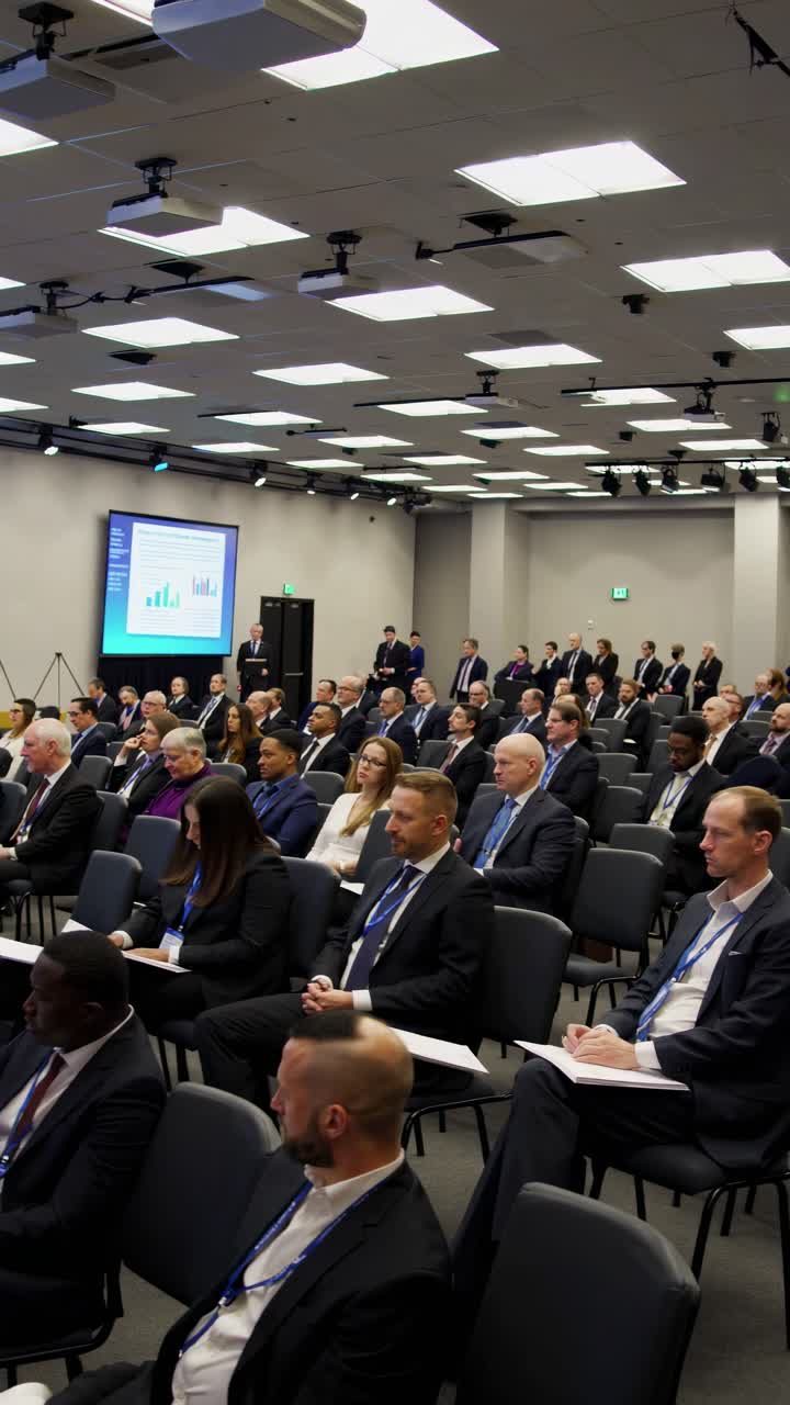 Diverse professionals gathering around conference table, focusing on presenter delivering insights via large projection screen during corporate strategy session