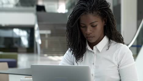 concentrated young woman with dreadlocks typing on laptop