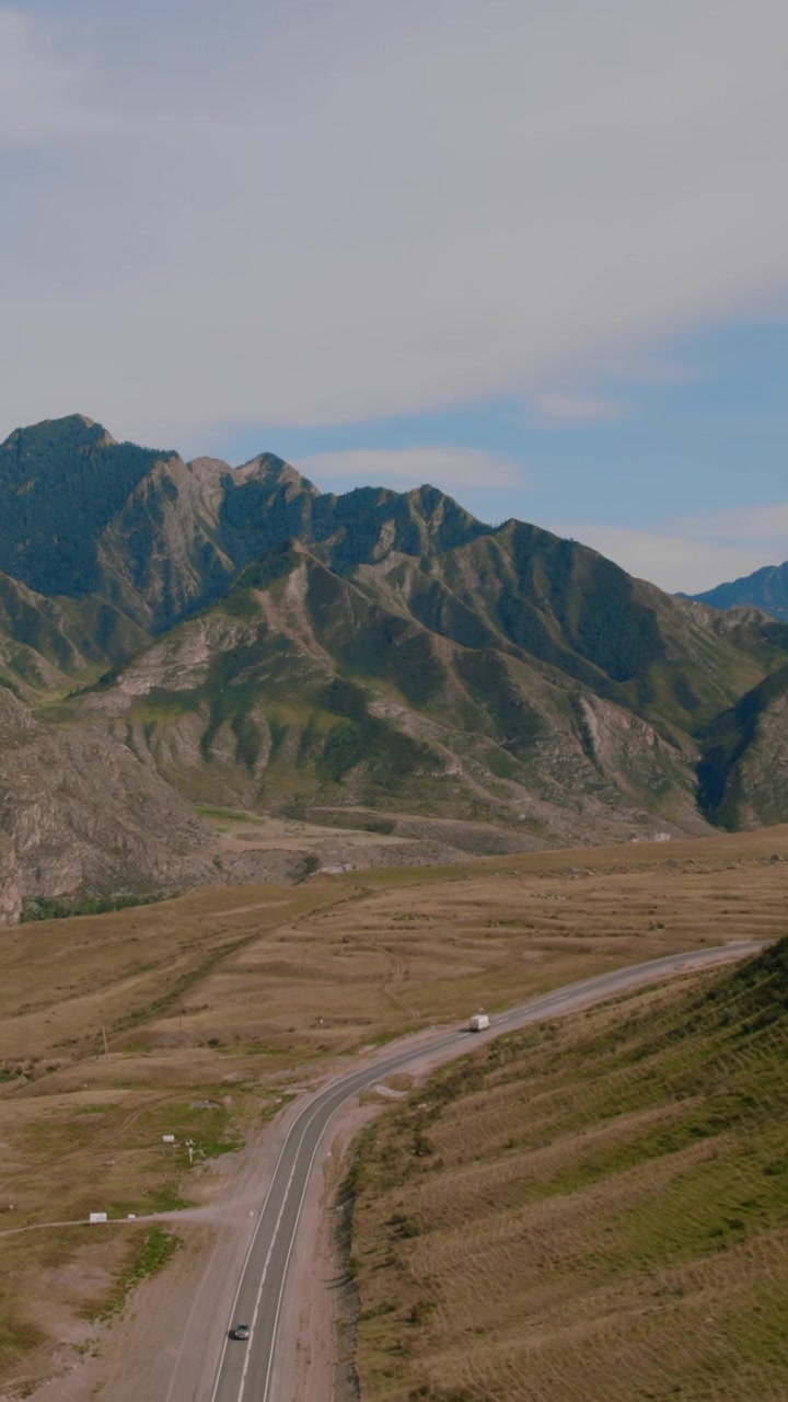 Riprese aeree con drone della strada Chuysky Trakt che si snoda attraverso un'ampia valle di montagna con auto in transito. Paesaggio suggestivo nella Repubblica dell'Altai, Russia, sotto un cielo azzurro.