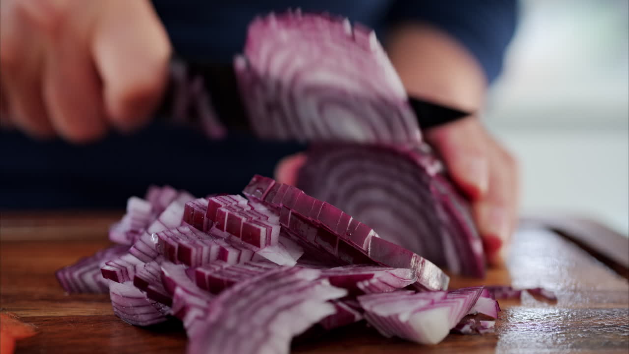 Close up of a woman cutting up a red onion near other vegetables on a wooden cutting board