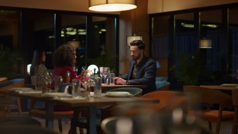 Young-couple-talk-together-at-restaurant-table.-Lovers-wait-dinner-food-in-cafe.