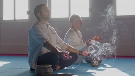 caucasian men meditating with incense in room