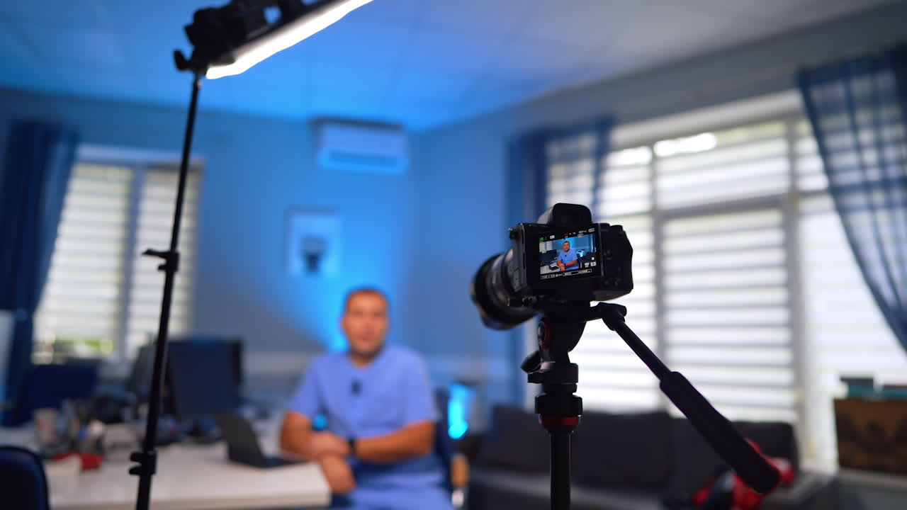 Digital camera and light directed on the Caucasian man in blue uniform. Professional doctor creates a video for a medical vlog. Selective focus