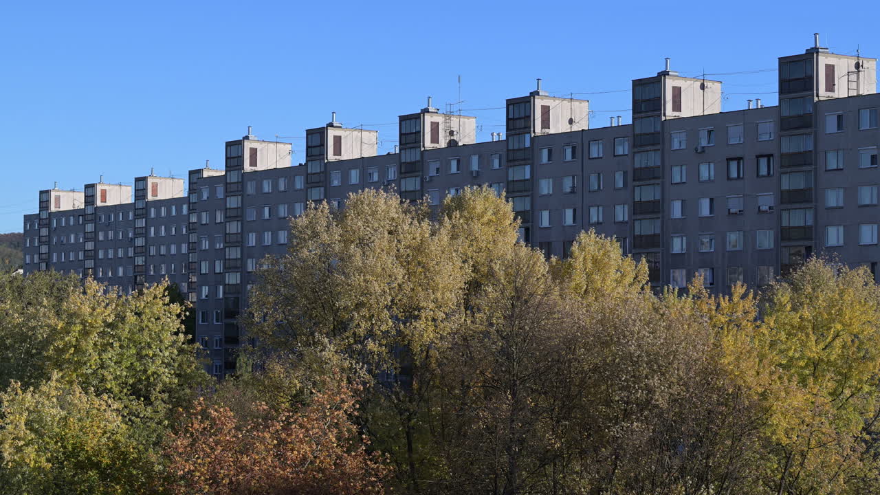 Brutalist apartment buildings behind autumn trees under blue sky