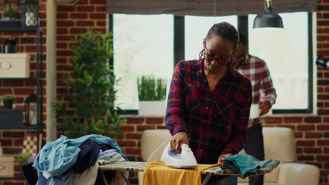 Adulto afroamericano che usa un ferro da stiro a vapore su un tavolo da stiro per le pulizie di primavera