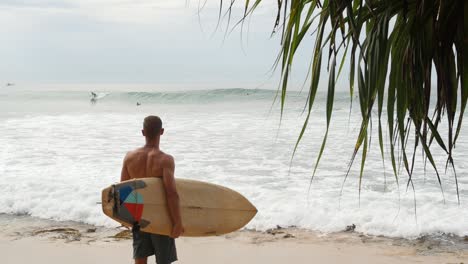 man surveying the waves from shore with surfboard in hand in sri lanka