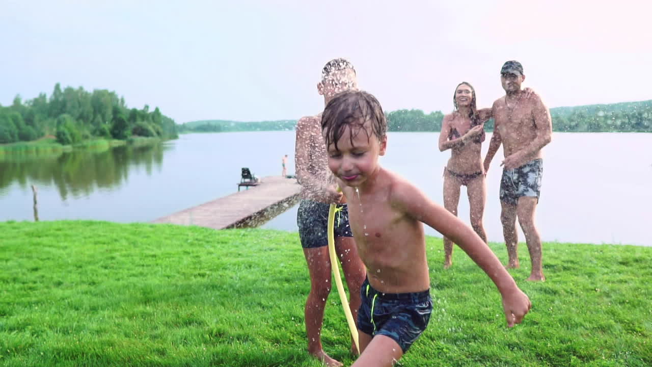 잔디 ⁇ 에서  ⁇ 은 여름날 두 아이와 함께 가족은 물로 놀고 웃으며 재미를 느 ⁇ 니다. 행복한 가족의 즐거운 분위기
